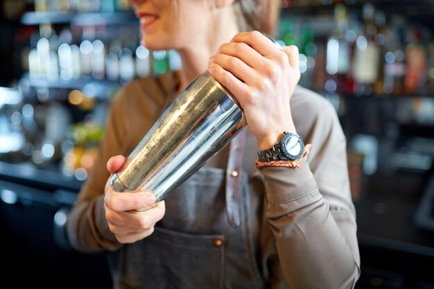 Woman bartender preparing cocktails using a silver shaker.