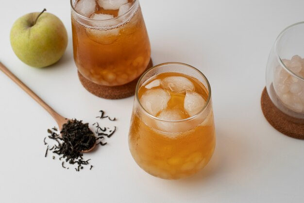 Two glasses of iced tea, a teaspoon with dried tea, and an apple.