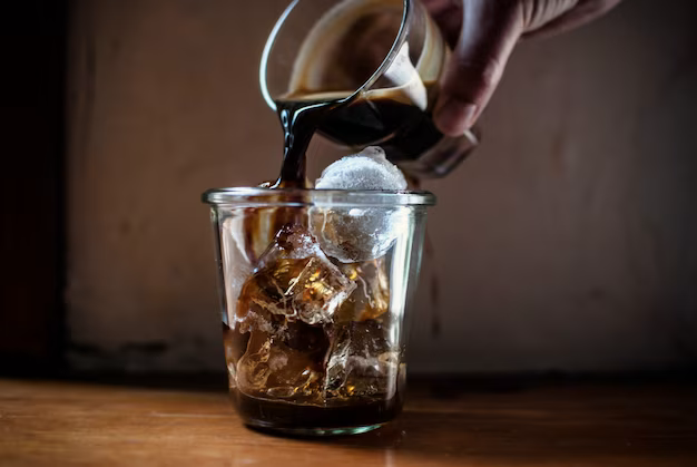 Hand pours coffee into a glass with ice